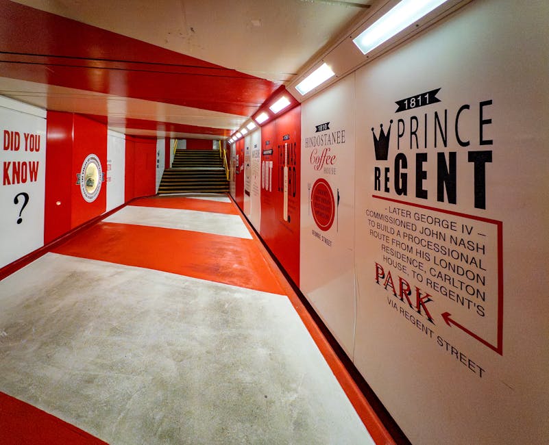 A clean, well-maintained underground passage with a polished concrete floor featuring a central red and white painted pathway. The walls are decorated with vintage-inspired signage and advertisements, including a prominent sign for Prince Regent and The Fidosstanee Coffee House, all in black and red lettering. The corridor is illuminated by bright overhead fluorescent lighting, creating a bright and tidy atmosphere. The stairs at the end of the passage indicate access to different levels. The overall appearance is one of cleanliness and recent maintenance, consistent with professional surface cleaning and upkeep by Cleaner Marylebone, ensuring hygiene and aesthetic appeal in a commercial or public space.